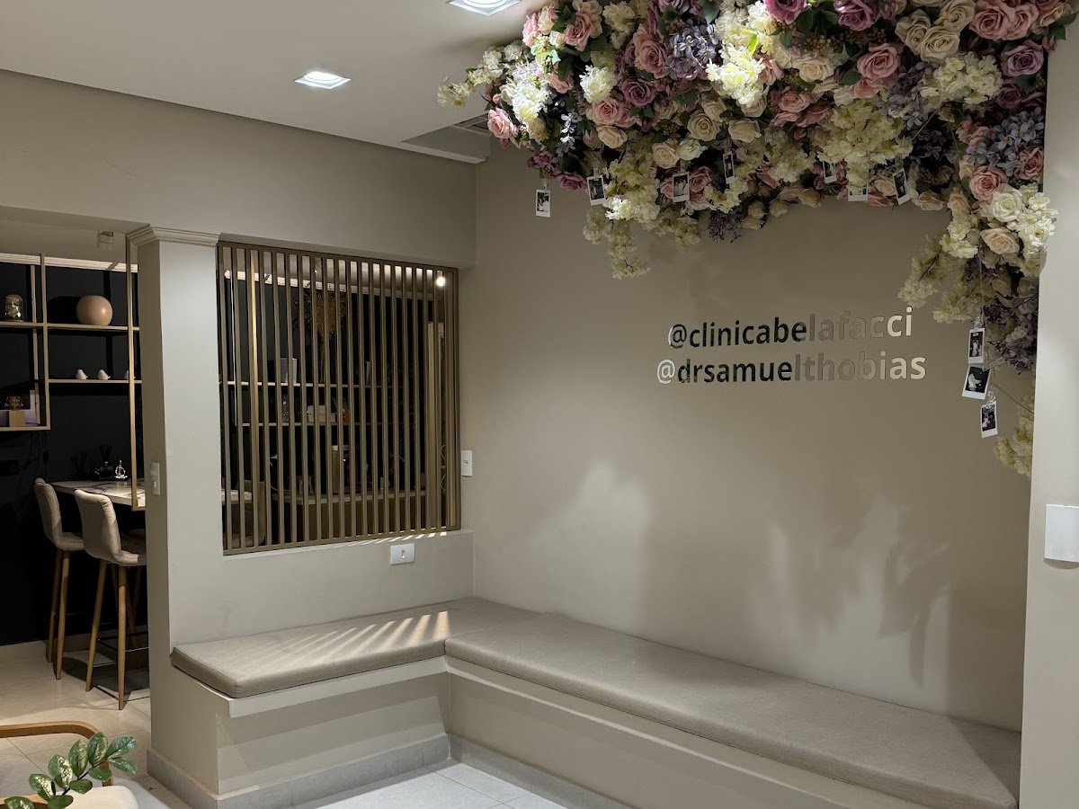 Recepção da Clínica Belafacci: banco greige em L, divisória metálica dourada e flores suspensas.